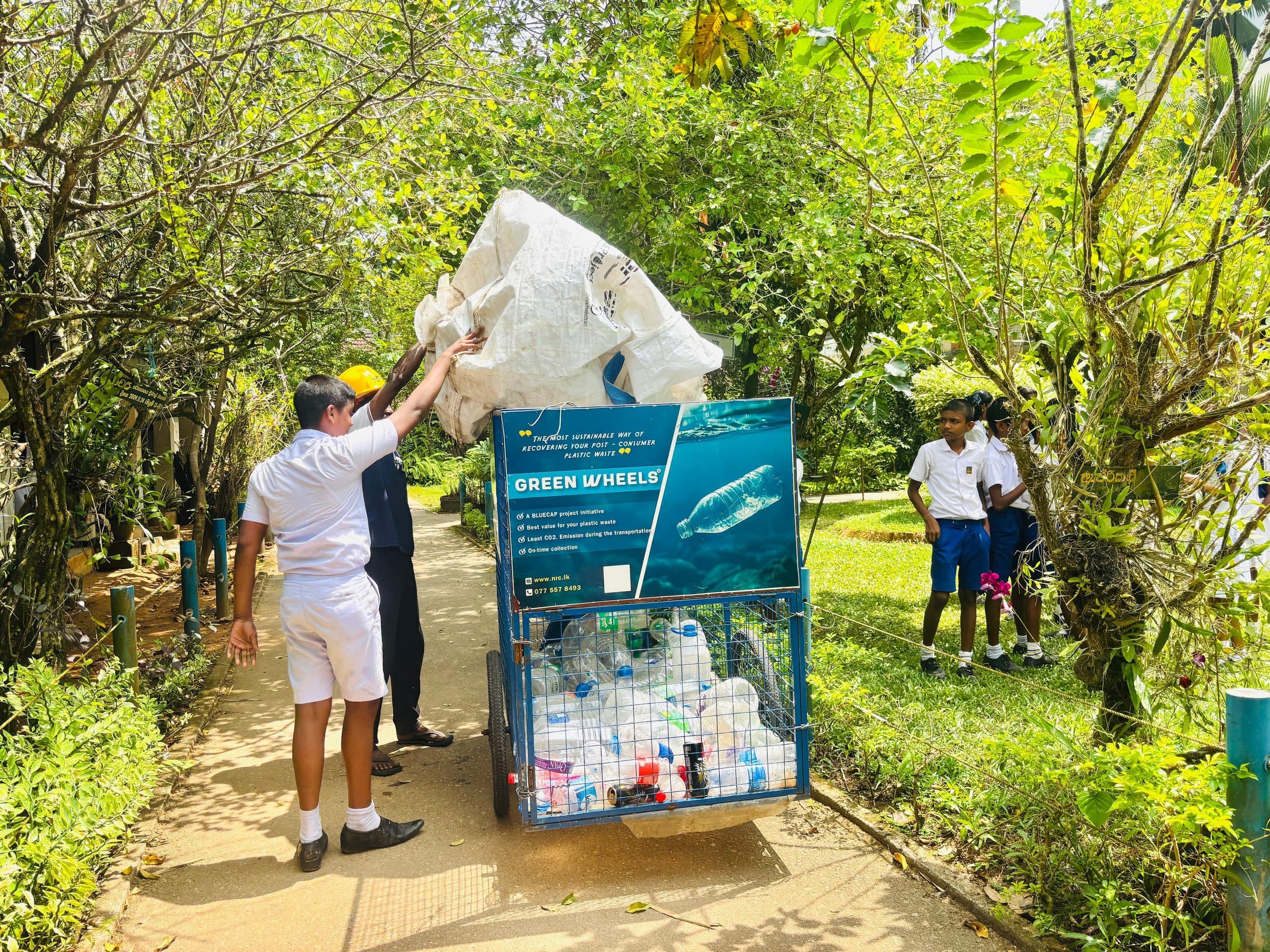 Emptying a bag of collected plastic into a Green Wheels collection cart during a BLUECAP school programme.
