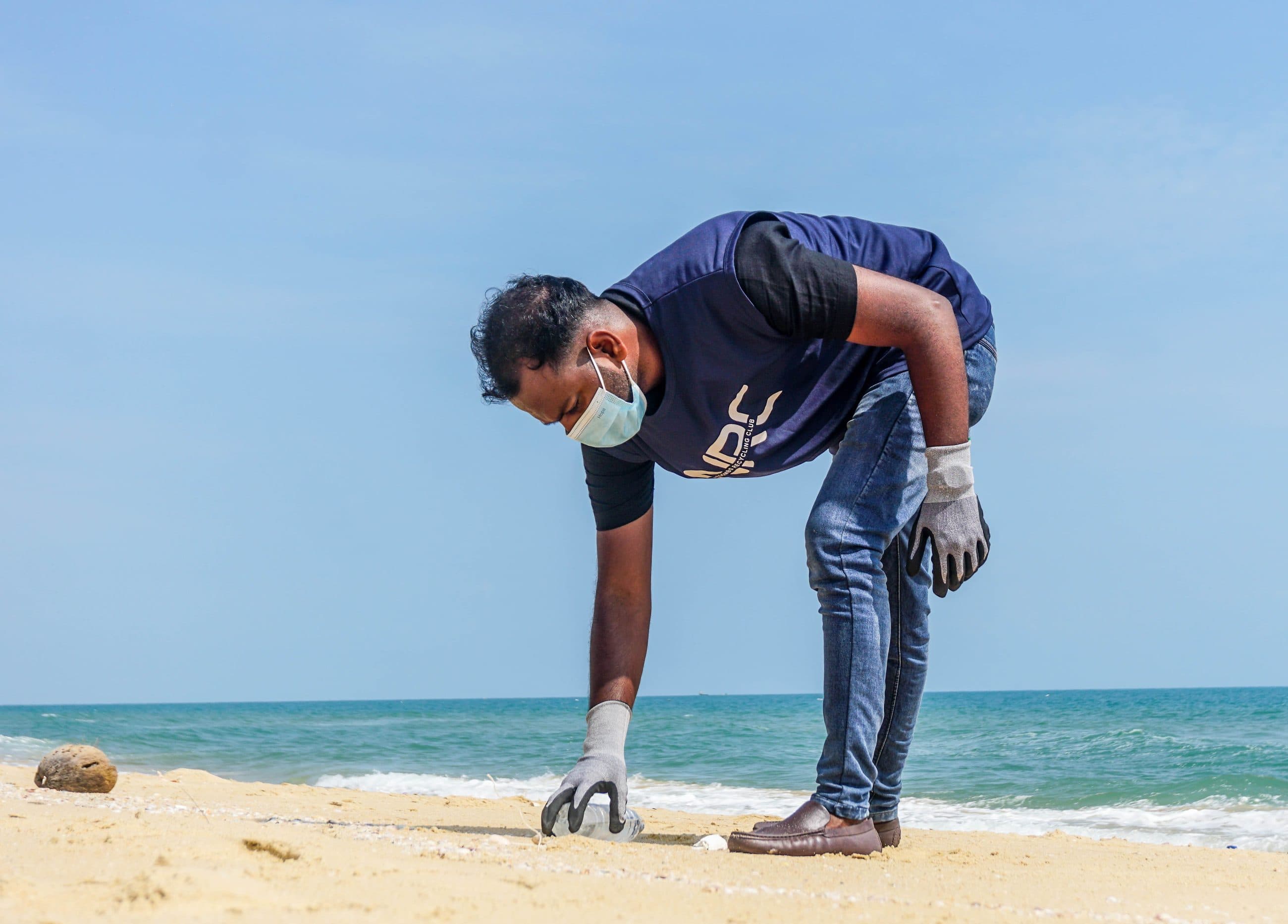 An NRC team member collecting plastic from the sand at the water's edge.