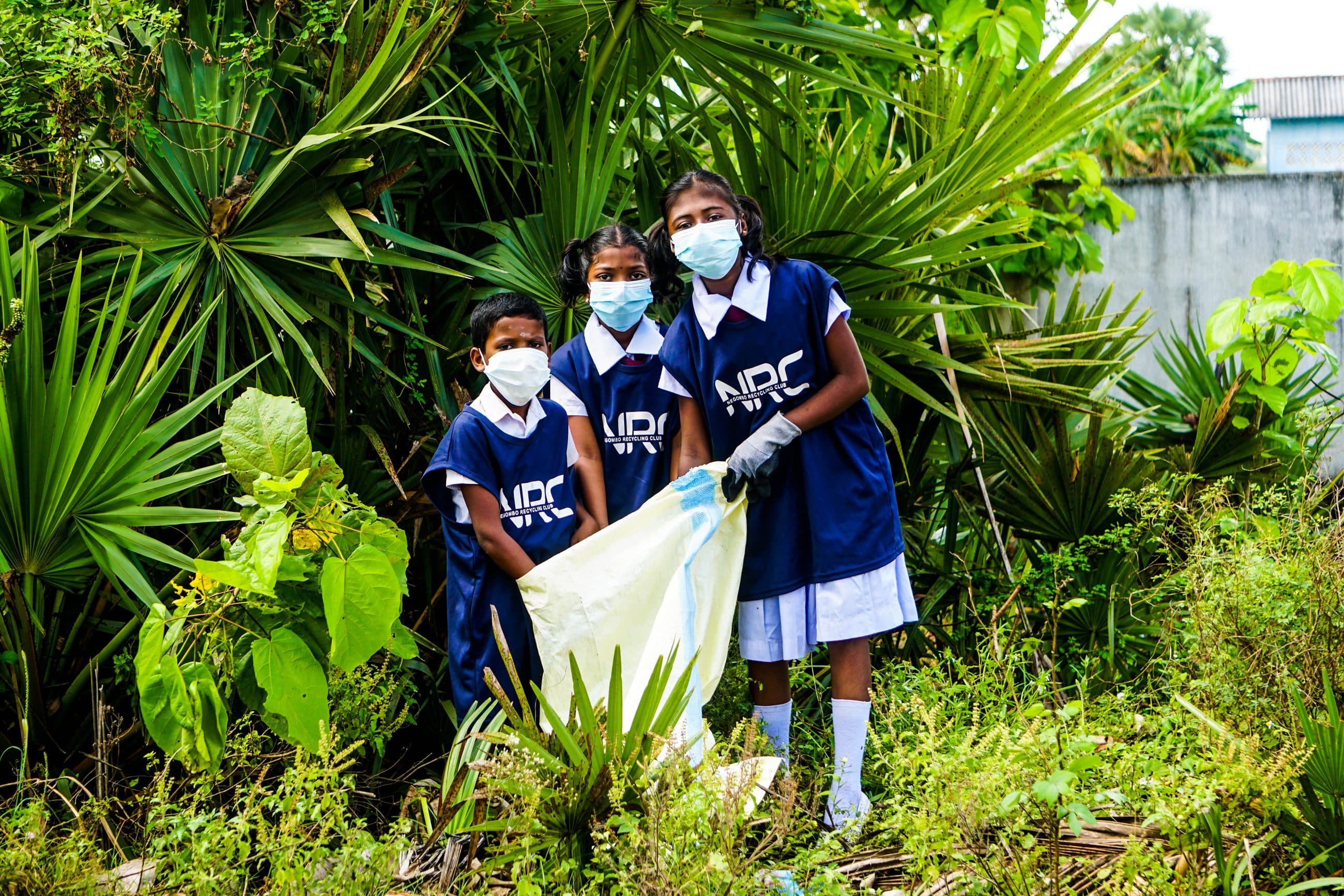 Three schoolchildren in NRC vests holding a collection bag together during a school cleanup.